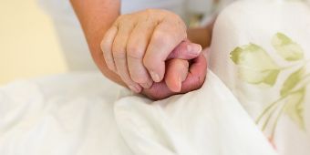 Zwei Menschen halten Hände Zuwendung am Patientenbett
